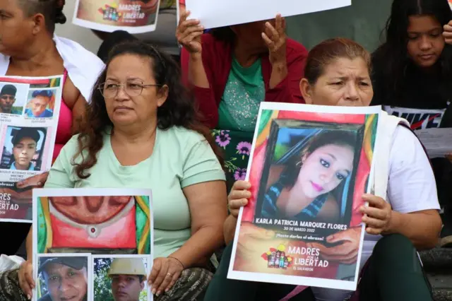 Liliana Urías (izquierda) y otras participantes del colectivo Madres por la Libertad sostienen carteles con imágenes de sus familiares detenidos durante una manifestación en las gradas de la catedral metropolitana en San Salvador, El Salvador.