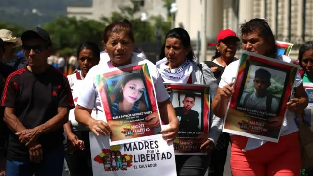Mujeres sostienen fotos de familiares detenidos durante el régimen de excepción en El Salvador y carteles en los que se lee "Madres por la Libertad" en el centro de San Salvador.