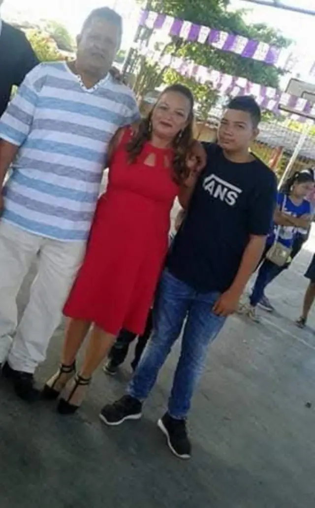 Fotografía de Liliana Urías, vestida de rojo, abrazada a su esposo, Israel Reyes, y su hijo, Merlon Urías.